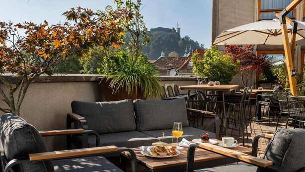 An outdoor seating area with tables and chairs, a sofa, and a view of a building in the background. - City Hotel Ljubljana (Ljubljana)