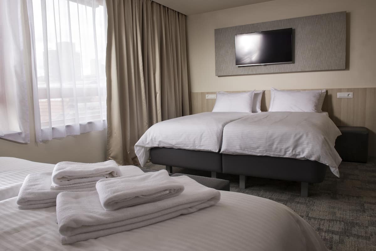 A hotel room with a large bed, a TV mounted on the wall, and a window with curtains.