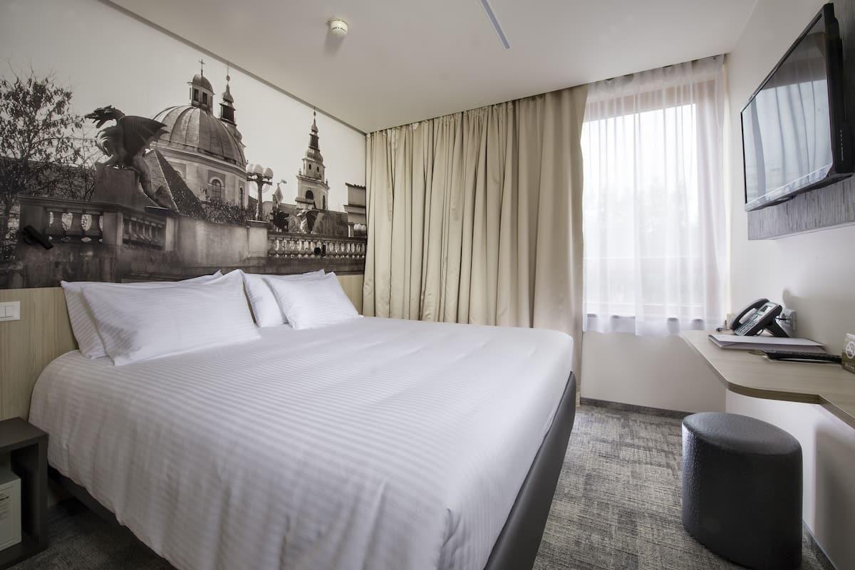 A hotel room with a large bed, a desk with a telephone, and a window with curtains.