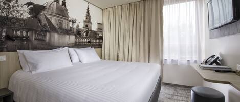A hotel room with a large bed, a desk with a telephone, and a window with curtains.