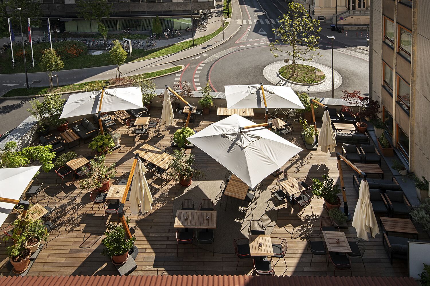An outdoor patio area with tables and chairs, surrounded by potted plants and umbrellas.