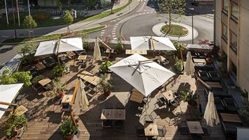 An outdoor patio area with tables and chairs, surrounded by potted plants and umbrellas.