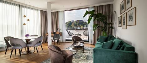 Een moderne woonkamer met een eethoek, grote ramen voorzien van gordijnen, een groene bank en uitzicht op een heuvel.