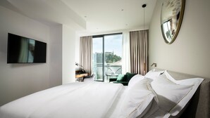 A modern hotel room with a large bed, a flat-screen TV, a desk with a chair, and a balcony with a view of a cityscape. - City Hotel Ljubljana (Ljubljana)