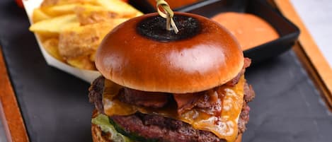 Ein Burger mit Zahnstocher, dazu Pommes und eine kleine Soße, alles auf einer Schieferplatte serviert.