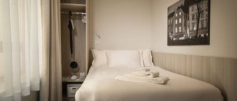 Habitación de hotel con una cama bien hecha, un armario, una mesita de noche con lámpara y un cuadro en la pared.