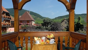 Un balcon en bois avec une table dressée pour le petit-déjeuner, offrant une vue sur un paysage rural avec des maisons et des collines.