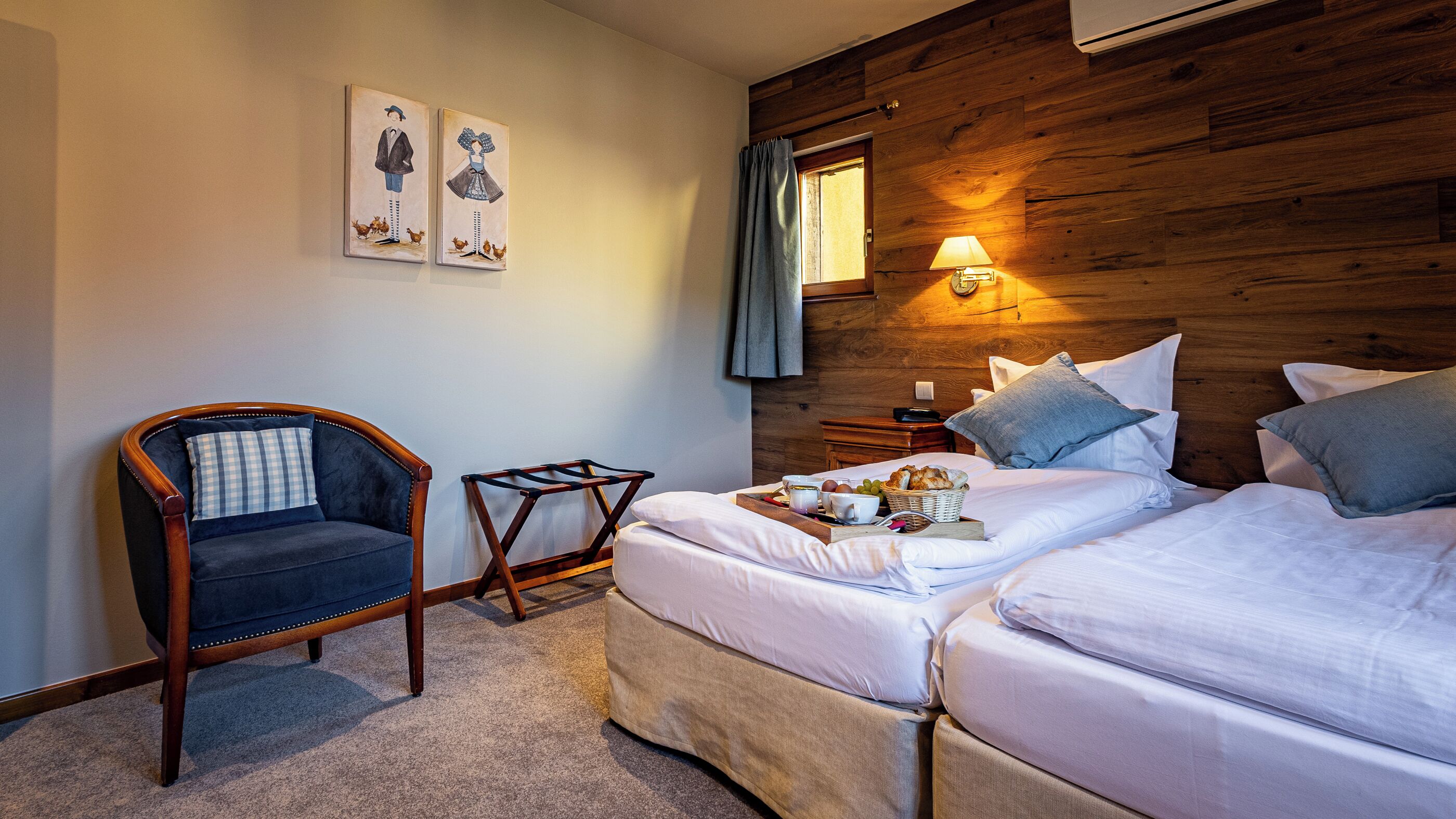 A hotel room with two beds, a wooden headboard, a chair, and artwork on the wall.