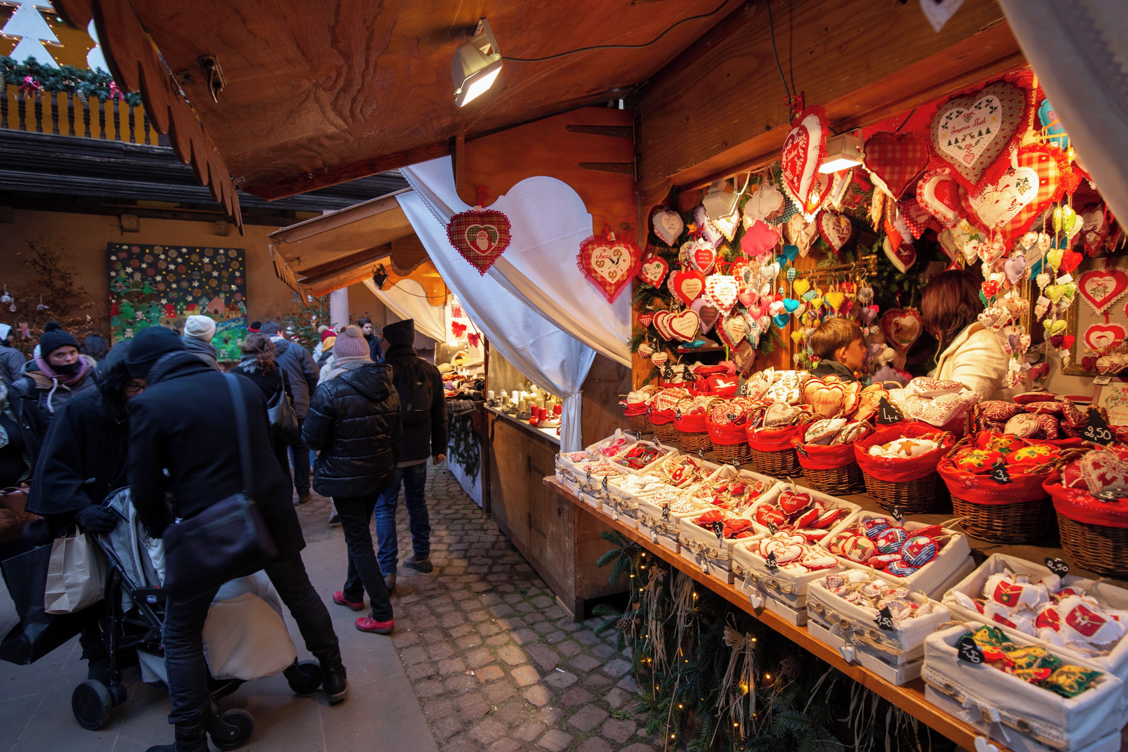 A crowded market with stalls selling various goods, including heart-shaped decorations and baskets.