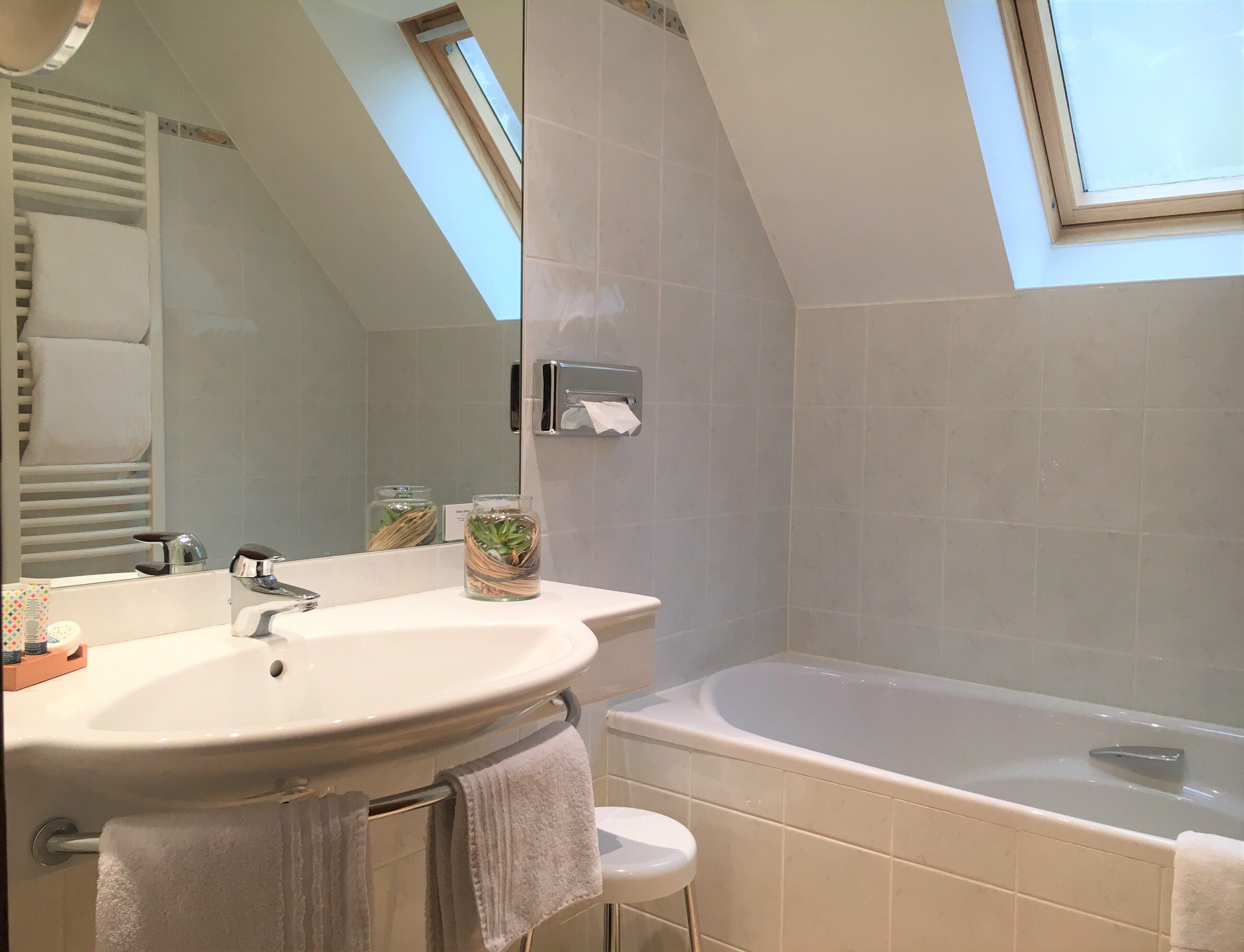 Un baño moderno con tragaluz, bañera, lavabo y espejo.
