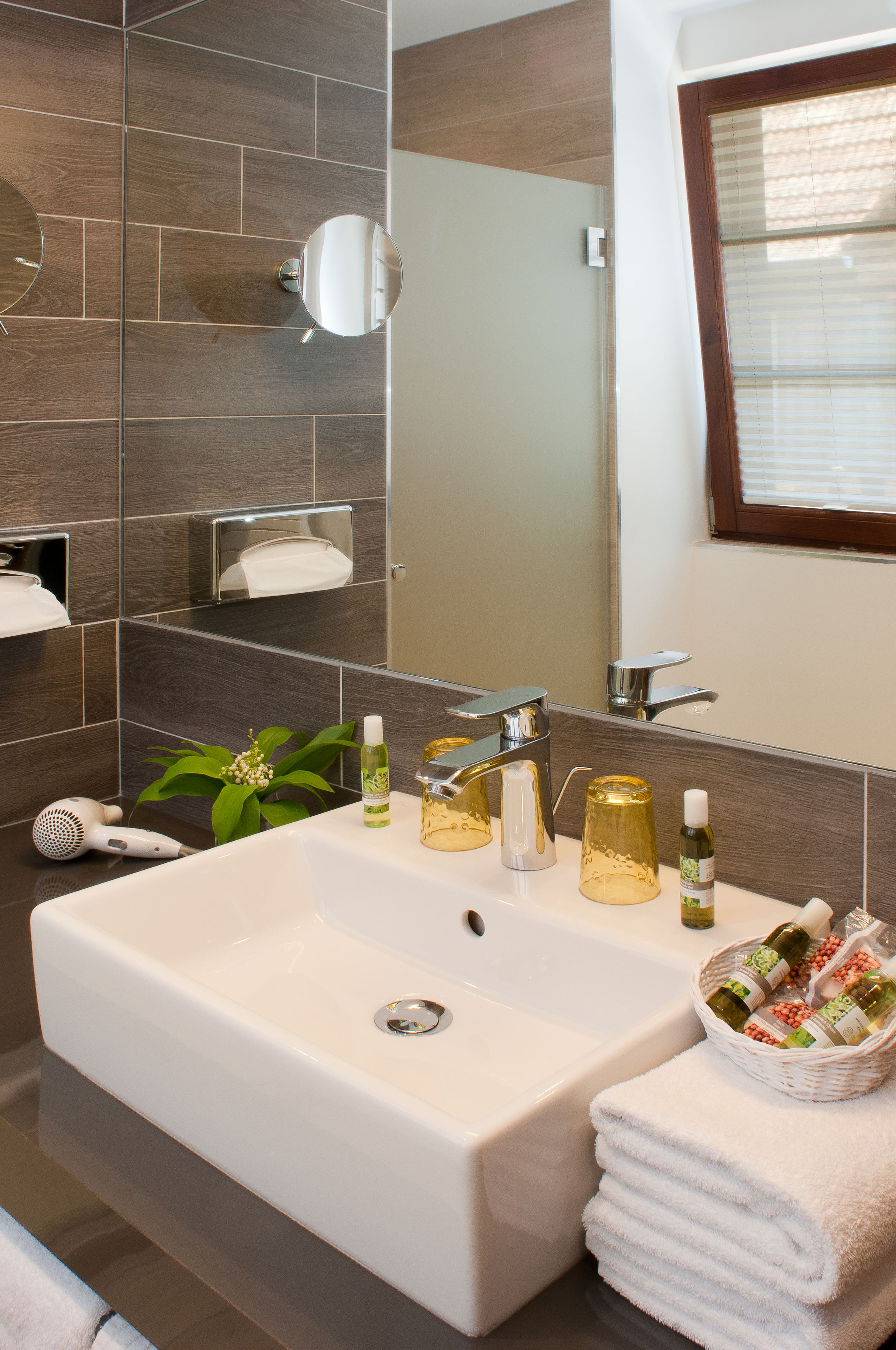 A bathroom with a large sink, a mirror, a towel rack, and a window with blinds.