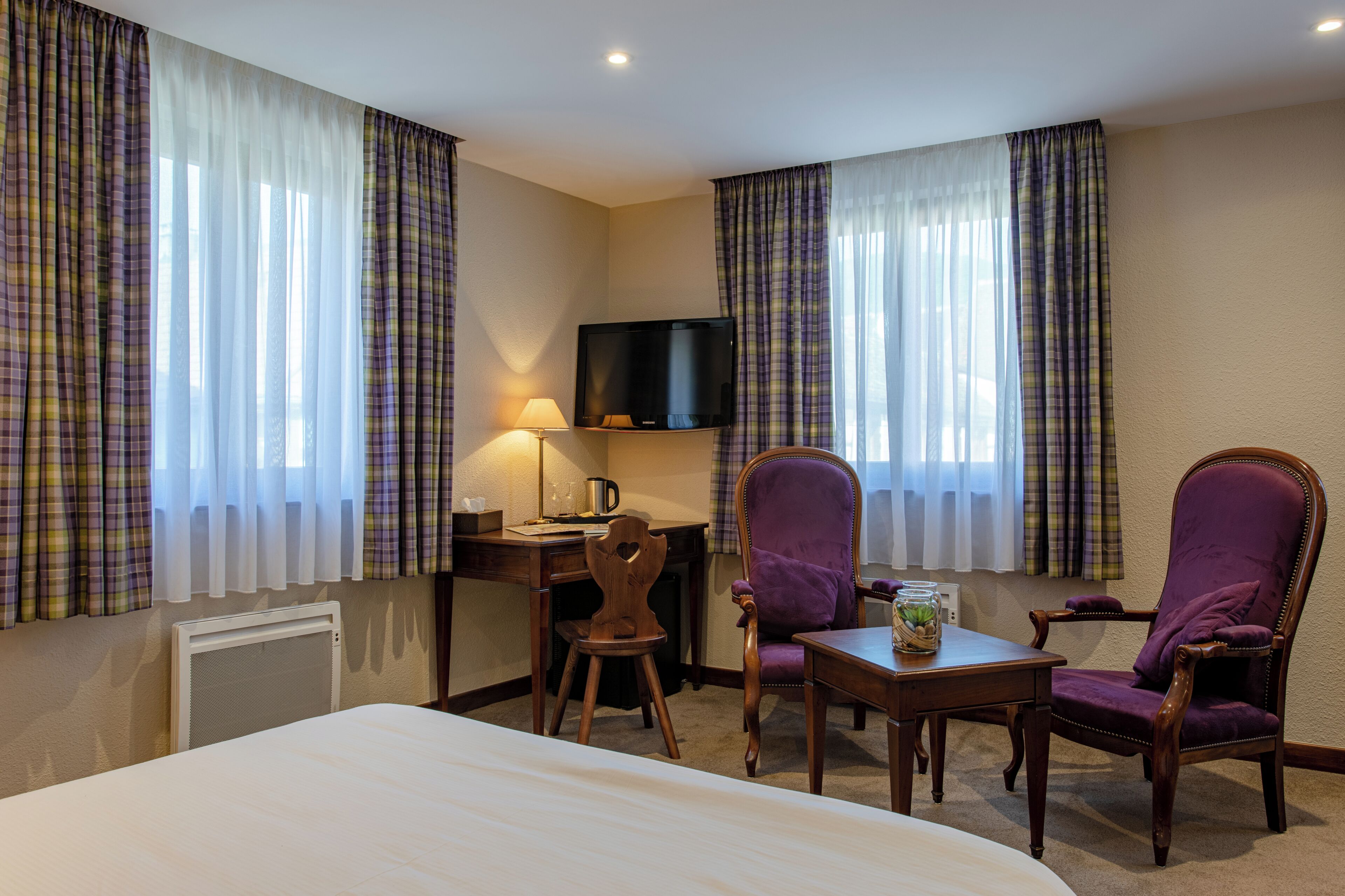 A hotel room with a bed, a desk, a chair, a television, and curtains.