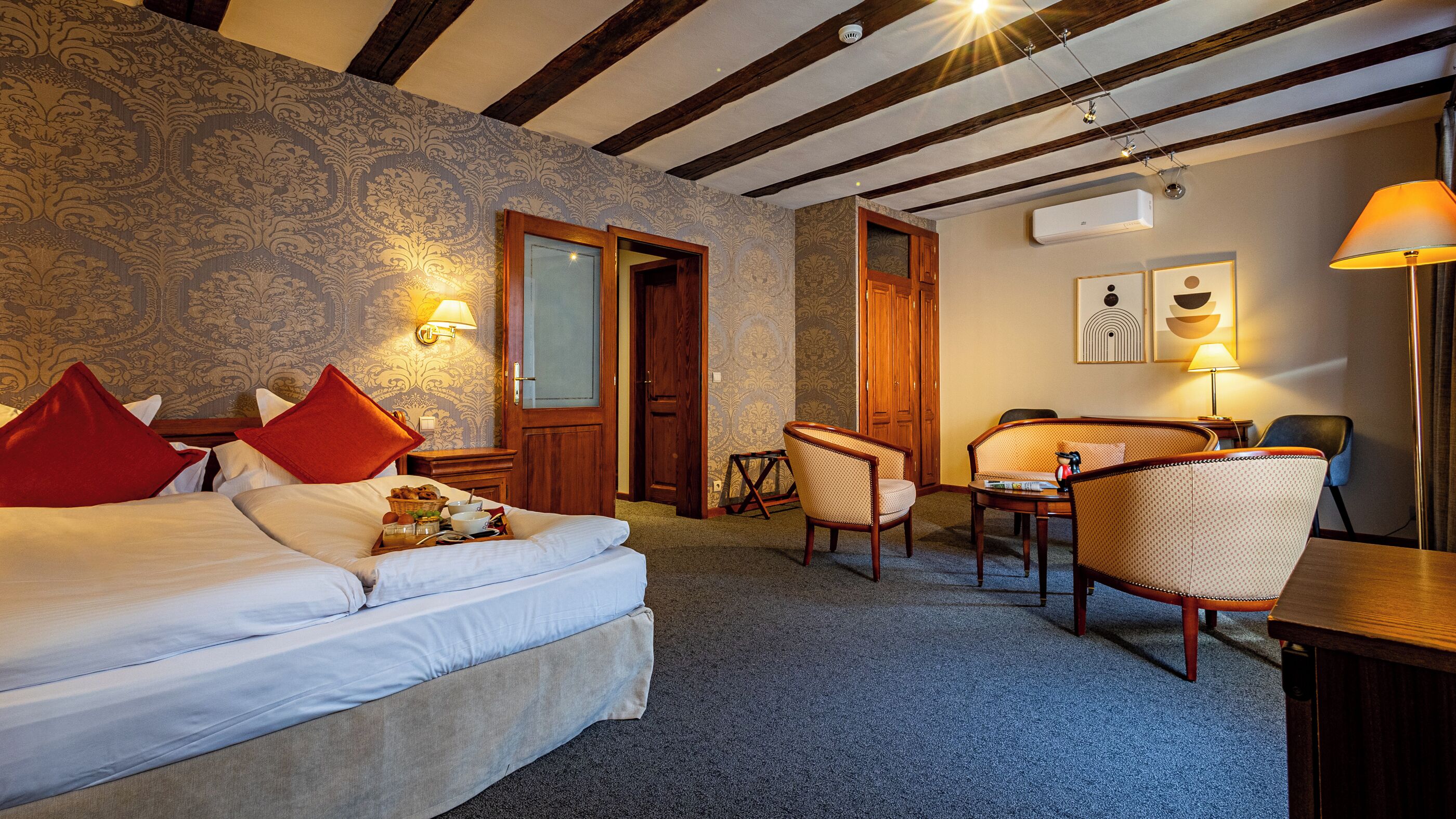 Een hotelkamer met een bed, een bureau, een stoel en een bank. Er zijn twee deuren, één naar de badkamer en één naar de gang.