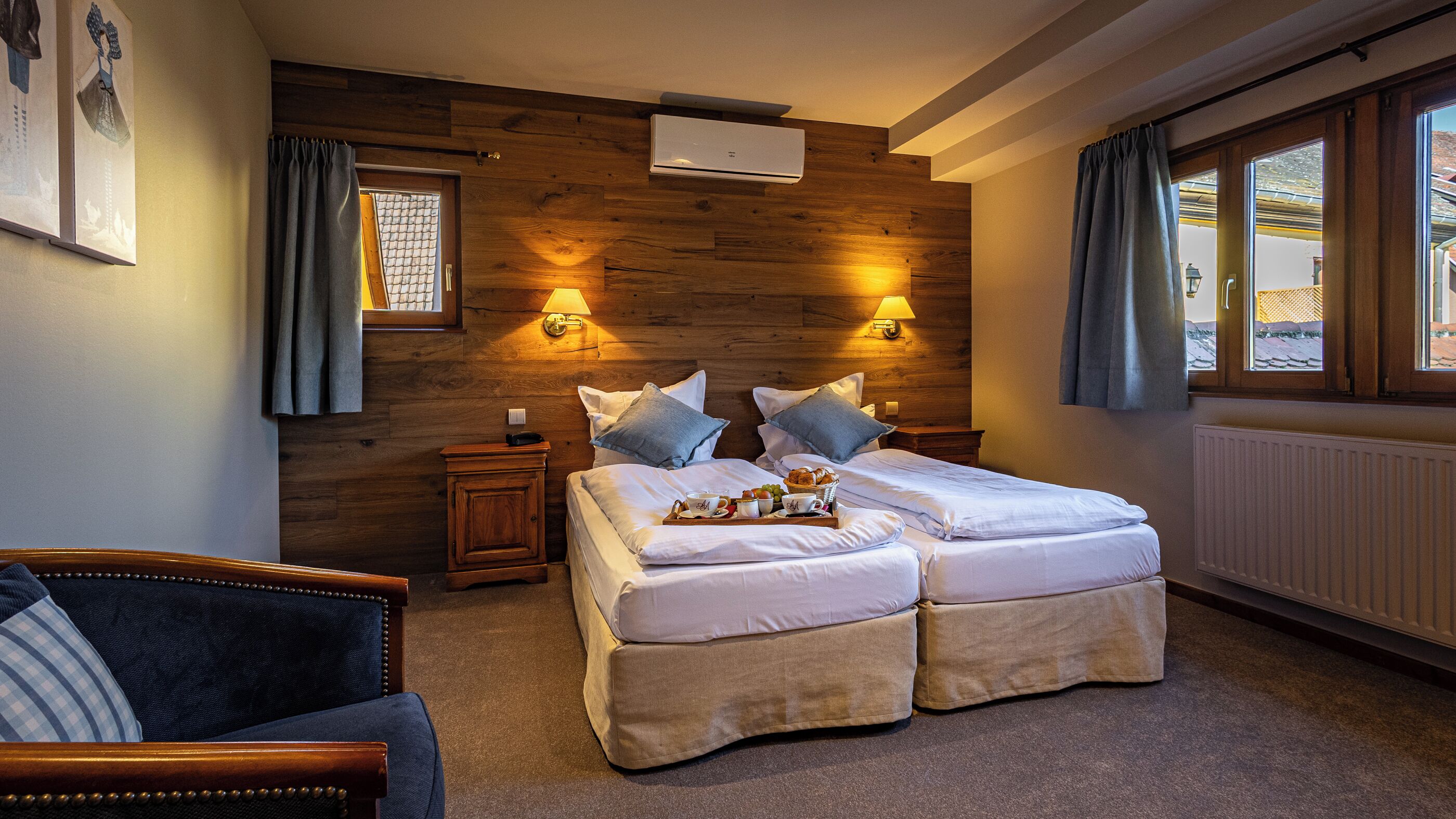 A double bed with two pillows, a bedside table, a lamp, and a tray with breakfast items.
