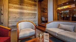Une pièce chaleureuse aux murs lambrissés, avec un canapé, un fauteuil et une table sur laquelle se trouvent une bouteille et un panneau.