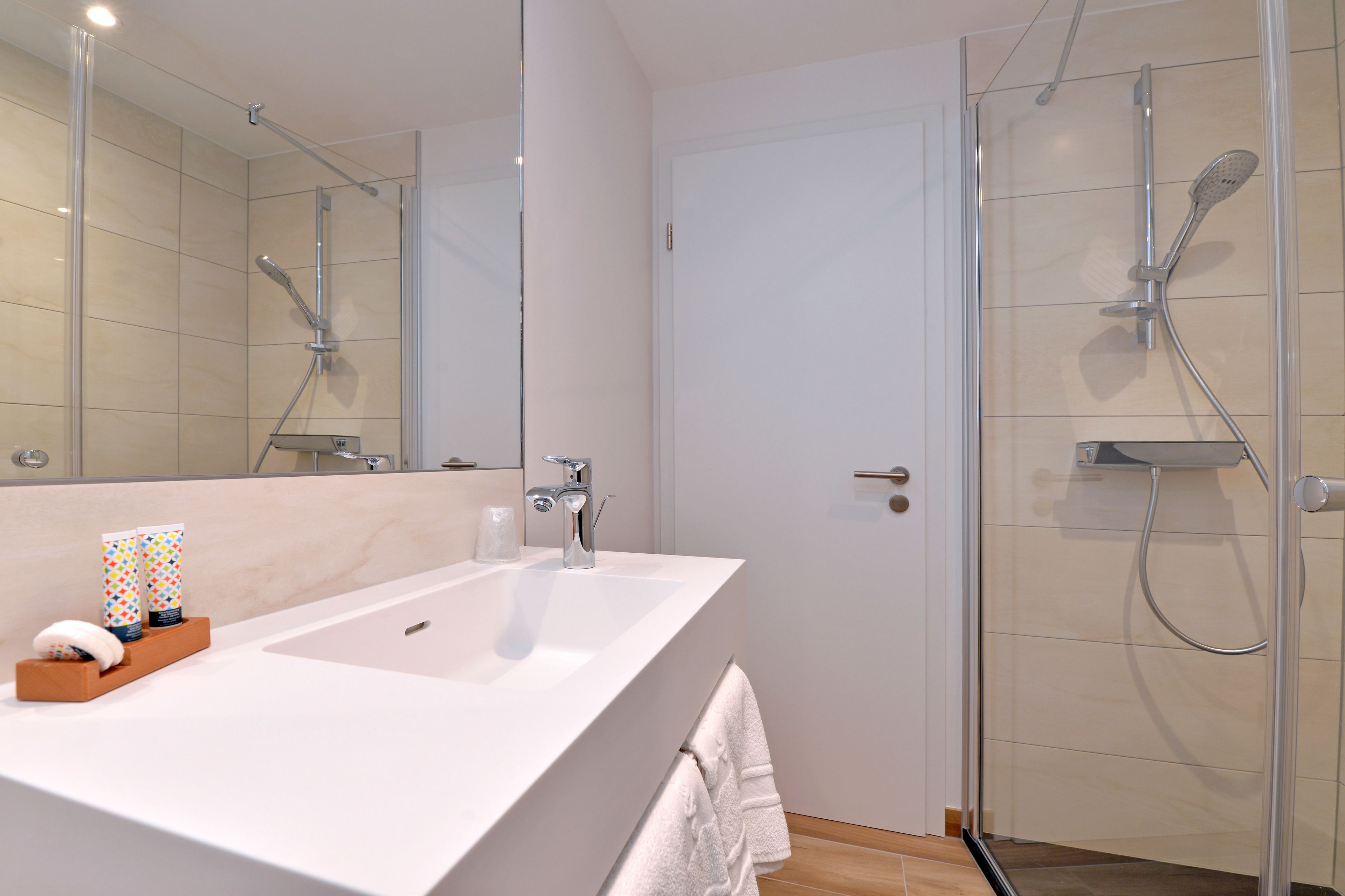 A modern bathroom with a large mirror, a white sink, and a glass-enclosed shower area.