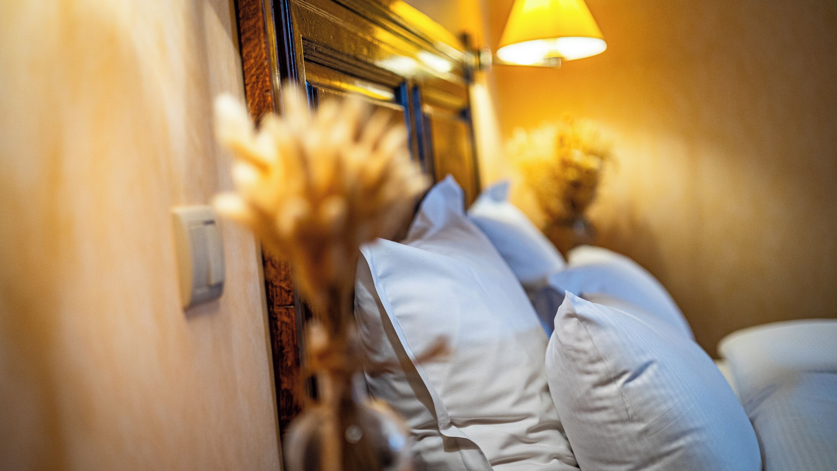 A close-up of a bed with white pillows and a lamp in the background.