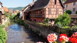 Une rivière traverse une ville où l’on trouve des maisons traditionnelles à colombages et un pont.