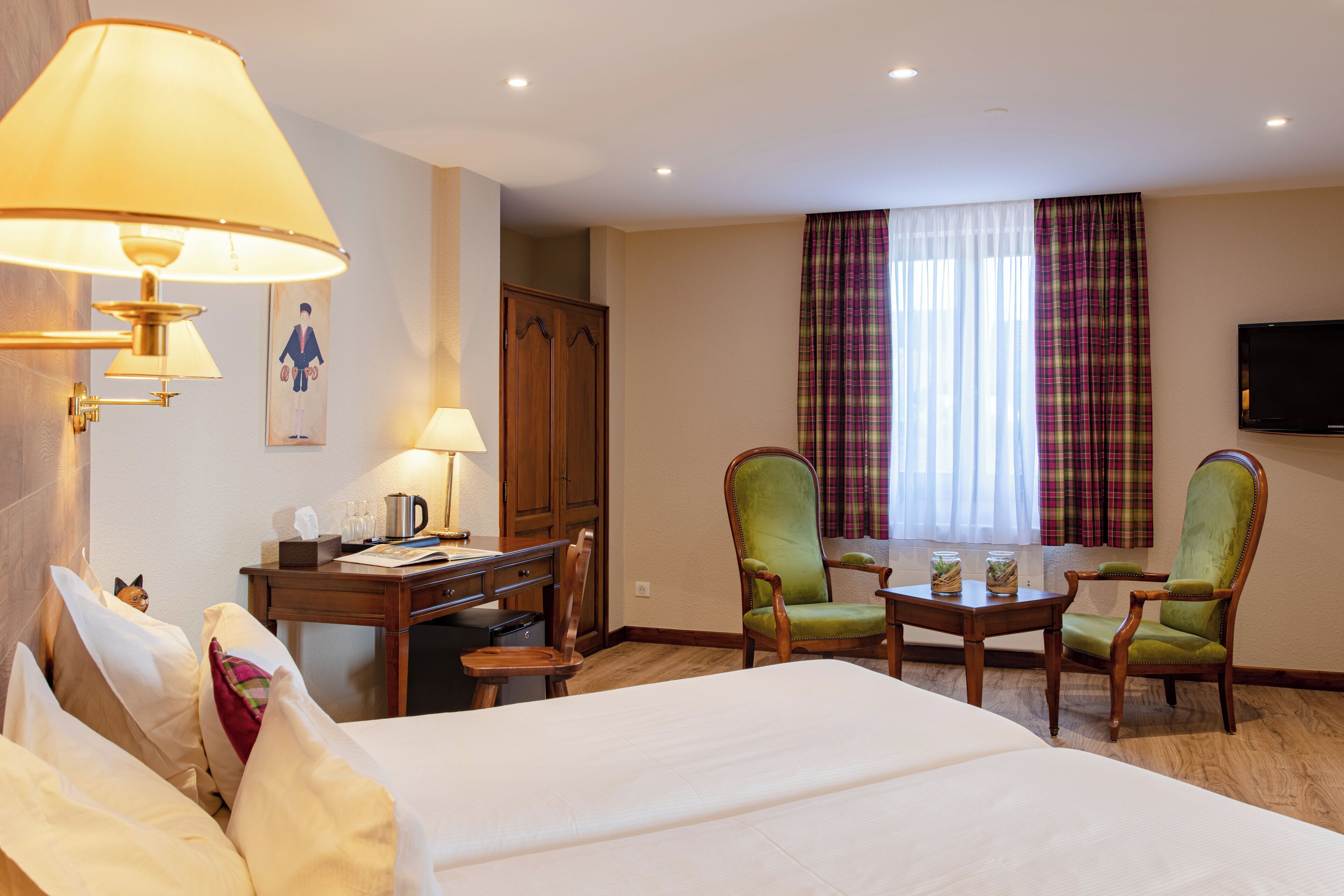 A hotel room with a bed, a desk, two chairs, a television, and a window with curtains.