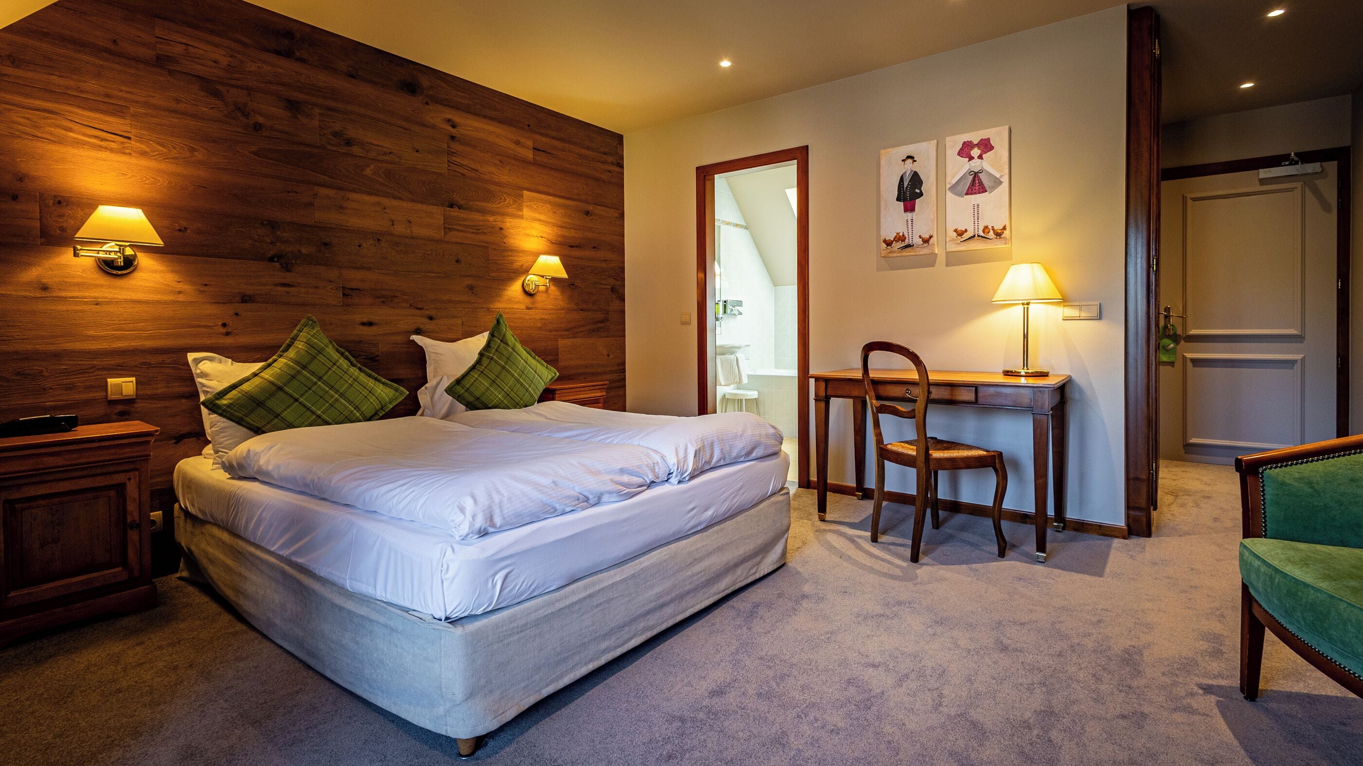 A hotel room with a wooden headboard, a bed with white linens, a desk with a chair, and two wall-mounted lamps.