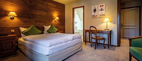A hotel room with a wooden headboard, a bed with white linens, a desk with a chair, and two wall-mounted lamps.