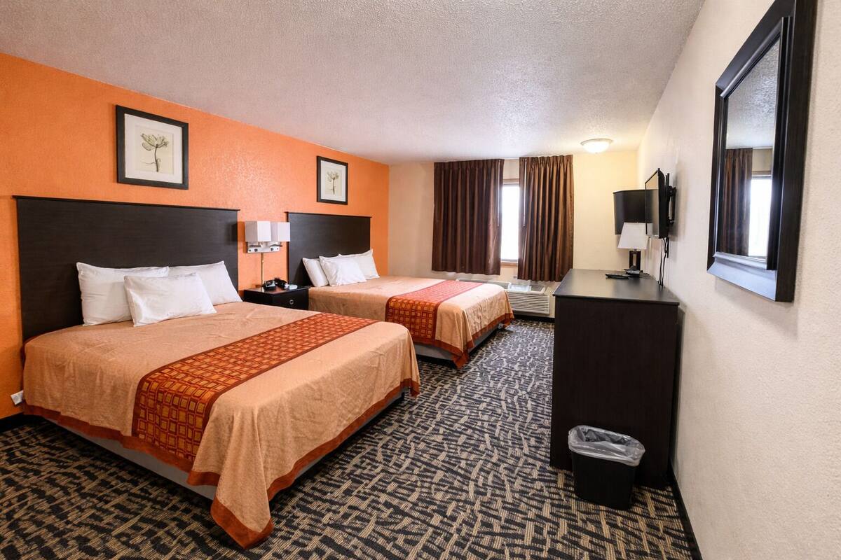 A hotel room with two beds, a desk, a trash bin, and a television.