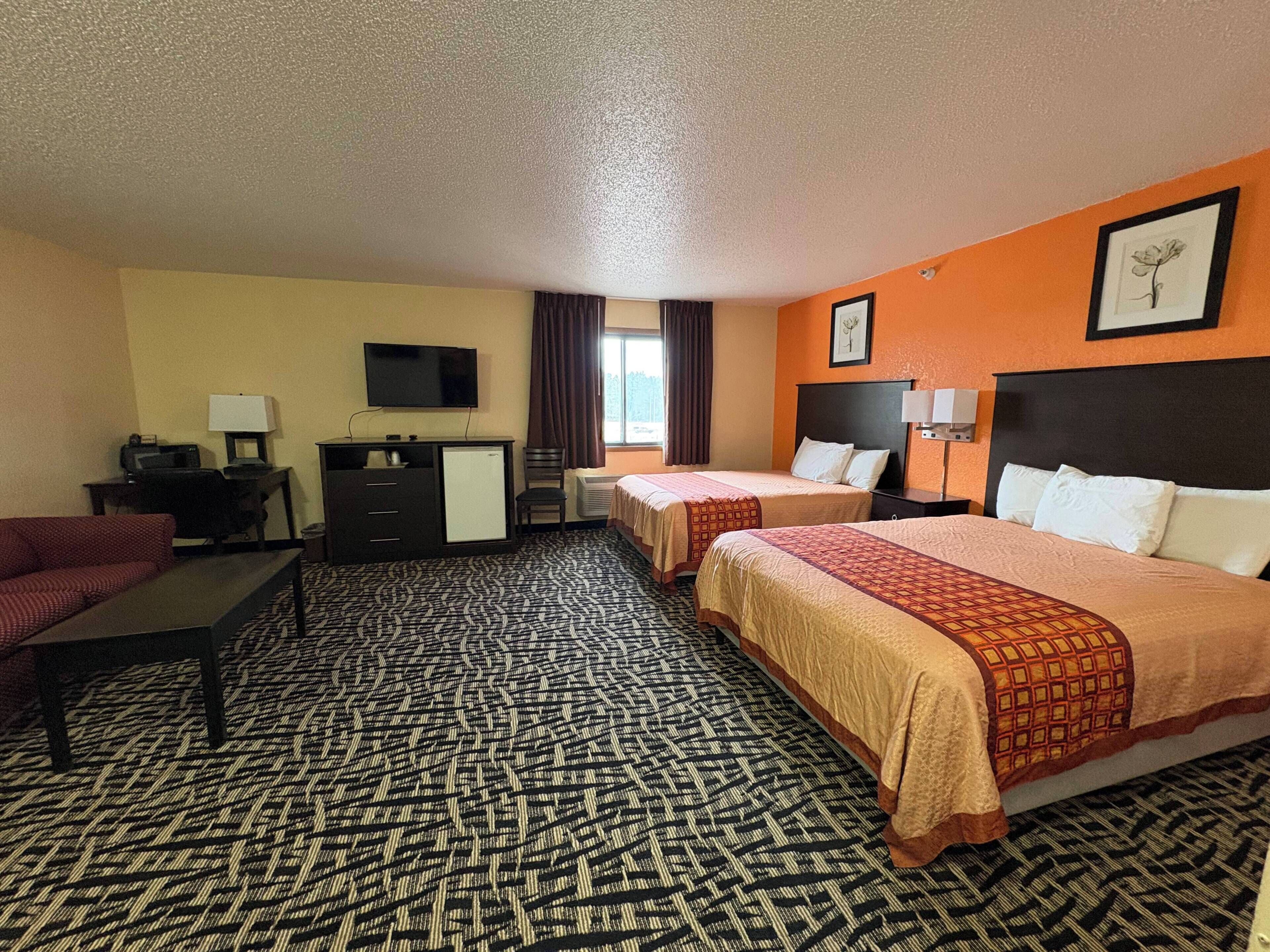 A hotel room with two beds, a desk with a computer, a TV, and a patterned carpet.