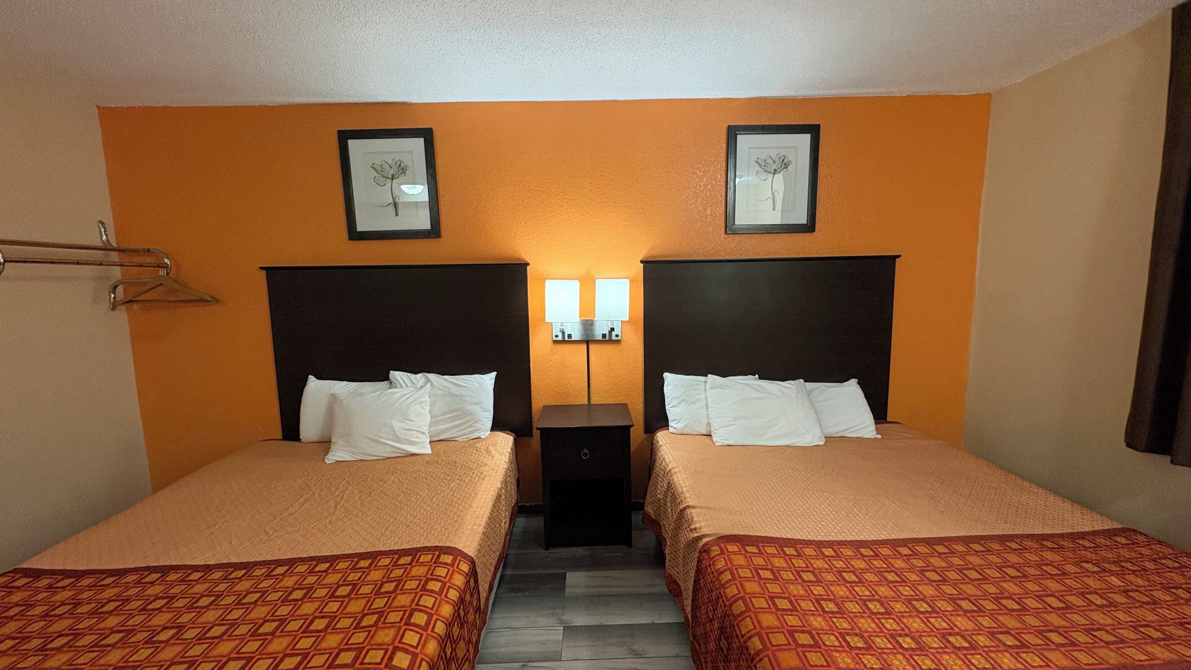 Et hotelværelse med to senge, et lille bord og en lampe fastgjort på væggen.