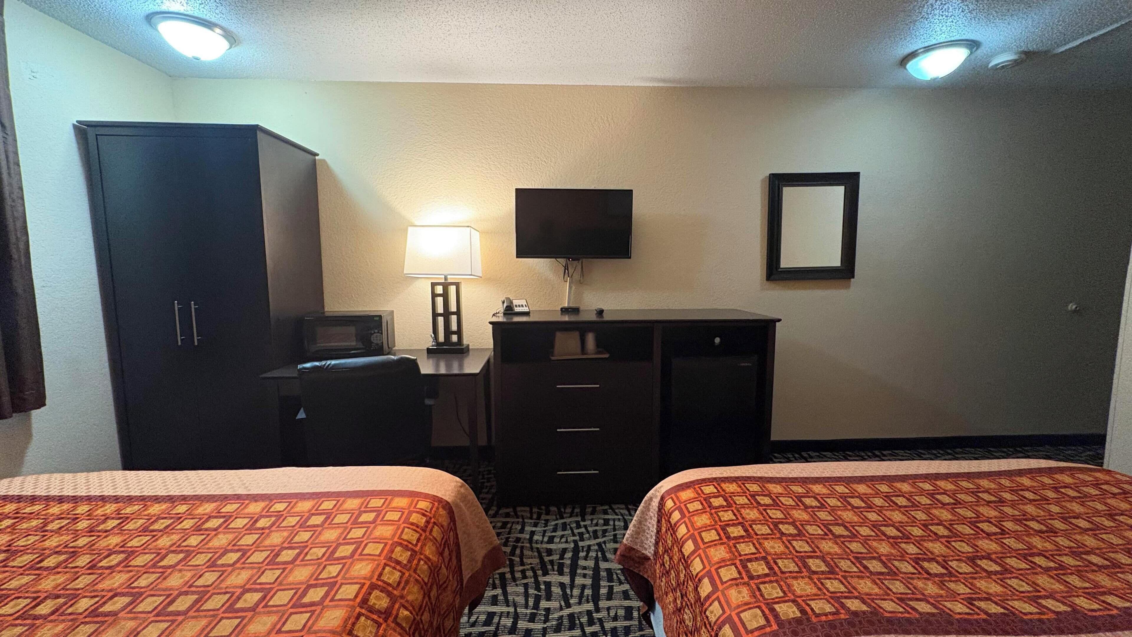A hotel room with two beds, a desk with a computer, a TV, and a wardrobe.