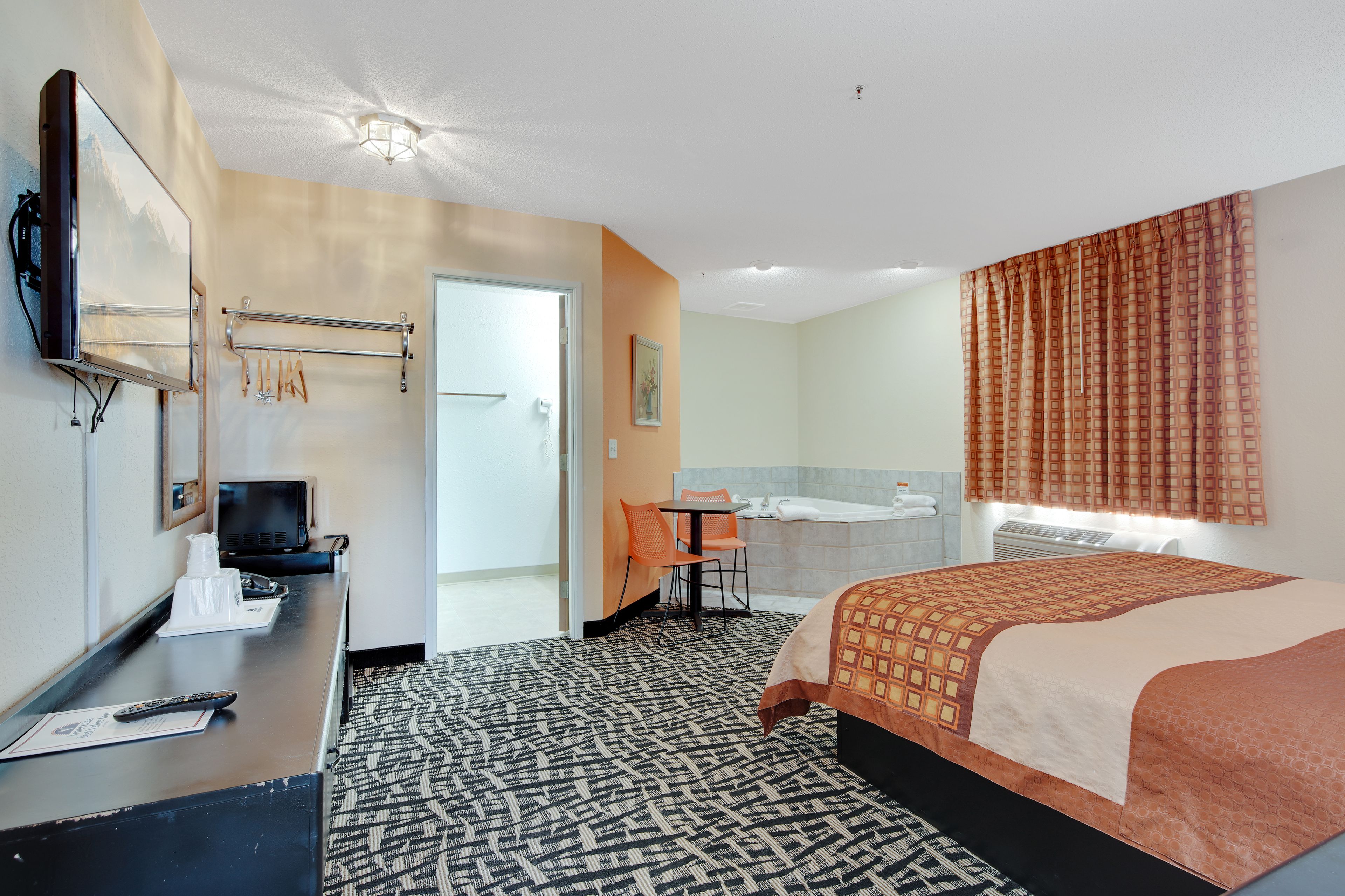 A hotel room with a bed, a desk with a computer, a TV, a bathroom with a bathtub, and a shower.