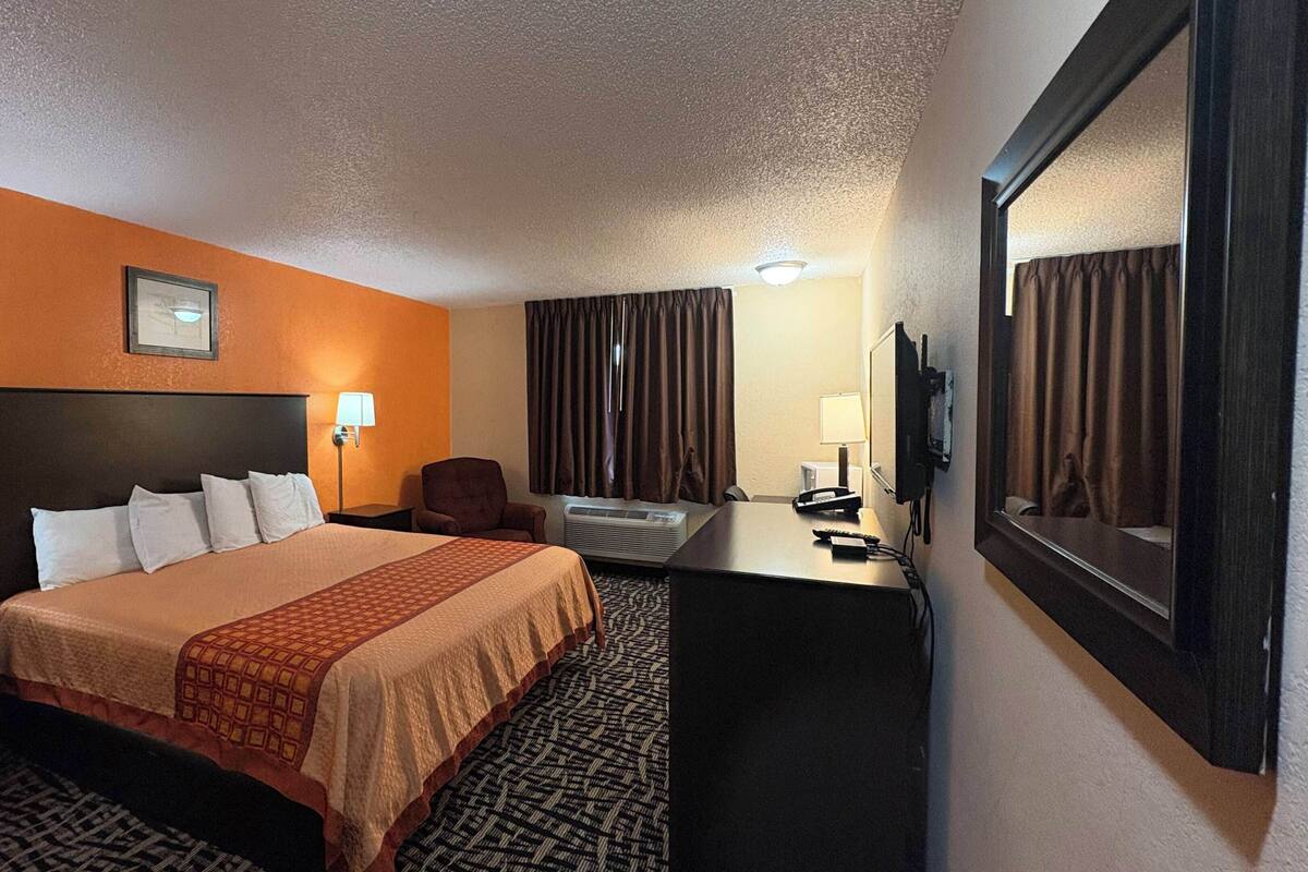A hotel room with a bed, desk, chair, TV, and two lamps.