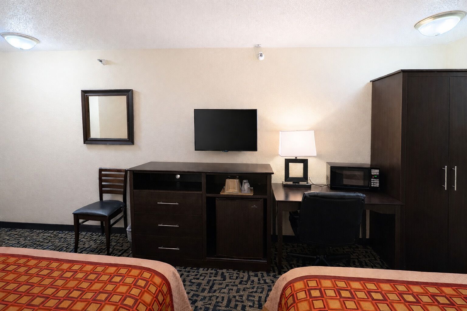 A hotel room with two beds, a desk with a chair, a television, a lamp, a microwave, and a wardrobe.