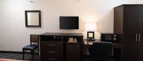 A hotel room with two beds, a desk with a chair, a television, a lamp, a microwave, and a wardrobe.