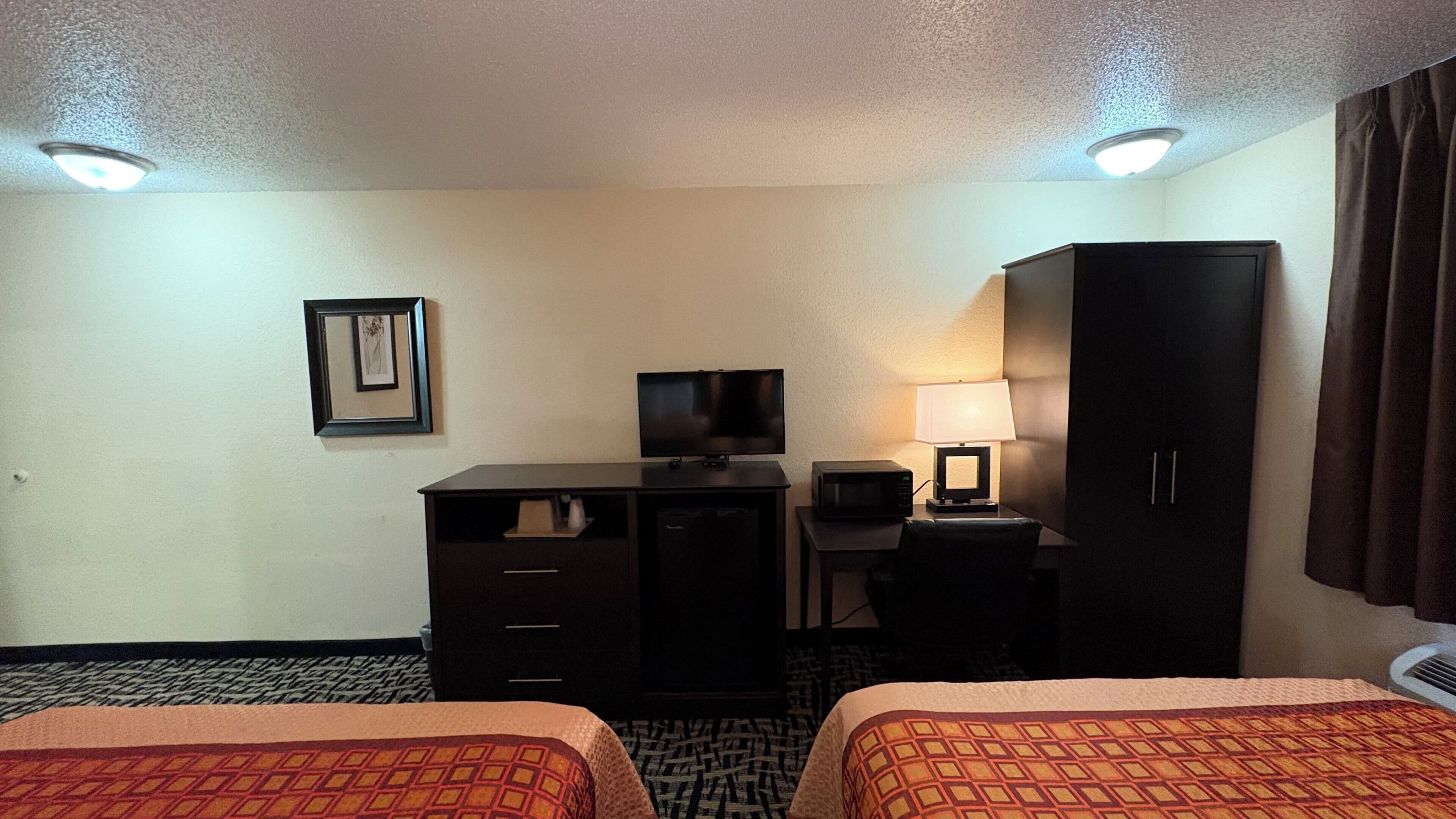 A hotel room with two beds, a desk, a television, a lamp, and a wardrobe.