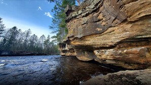 A rocky cliff by a river with trees in the background. - North Town Inn & Suites (Finlayson)