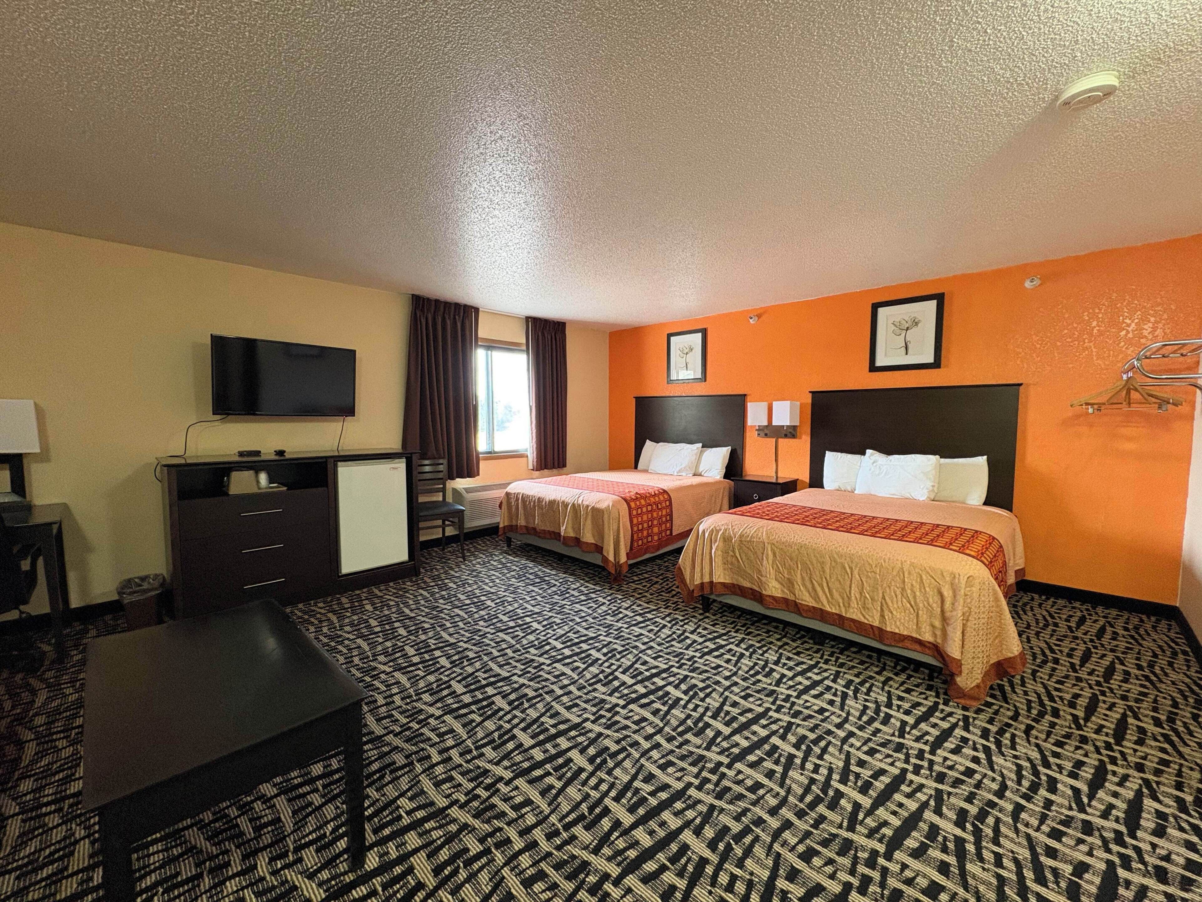 A hotel room with two beds, a desk, a television, and a window with curtains.