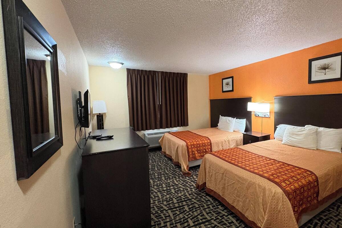 A hotel room with two beds, a desk, a TV, and a window with curtains.