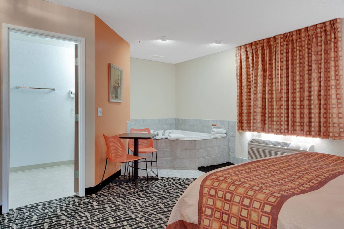 A hotel room with a bed, a bathroom with a bathtub, a table with two chairs, and a painting on the wall.