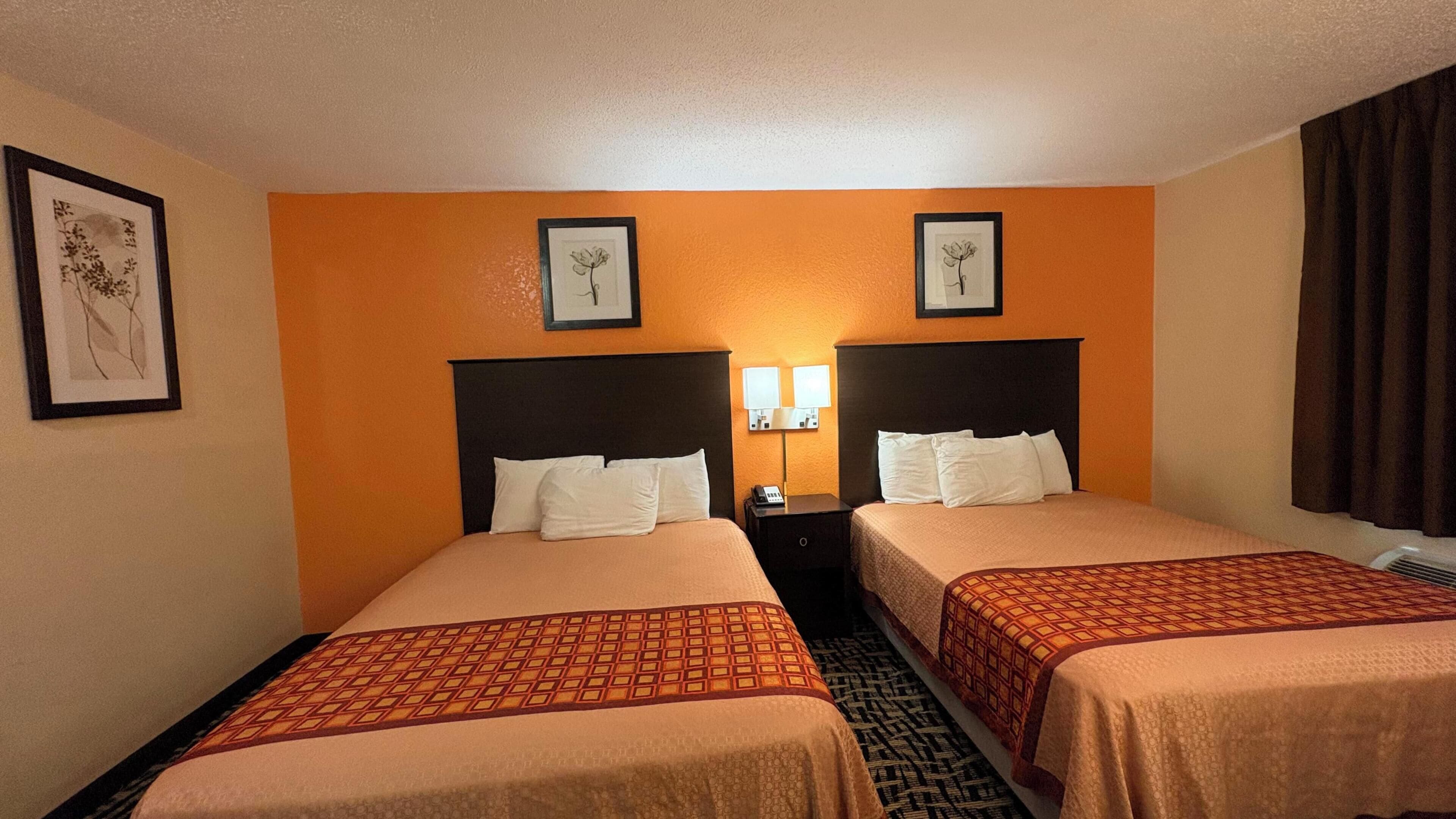 Habitación de hotel con dos camas, una mesita de noche con teléfono y obras de arte enmarcadas en las paredes.