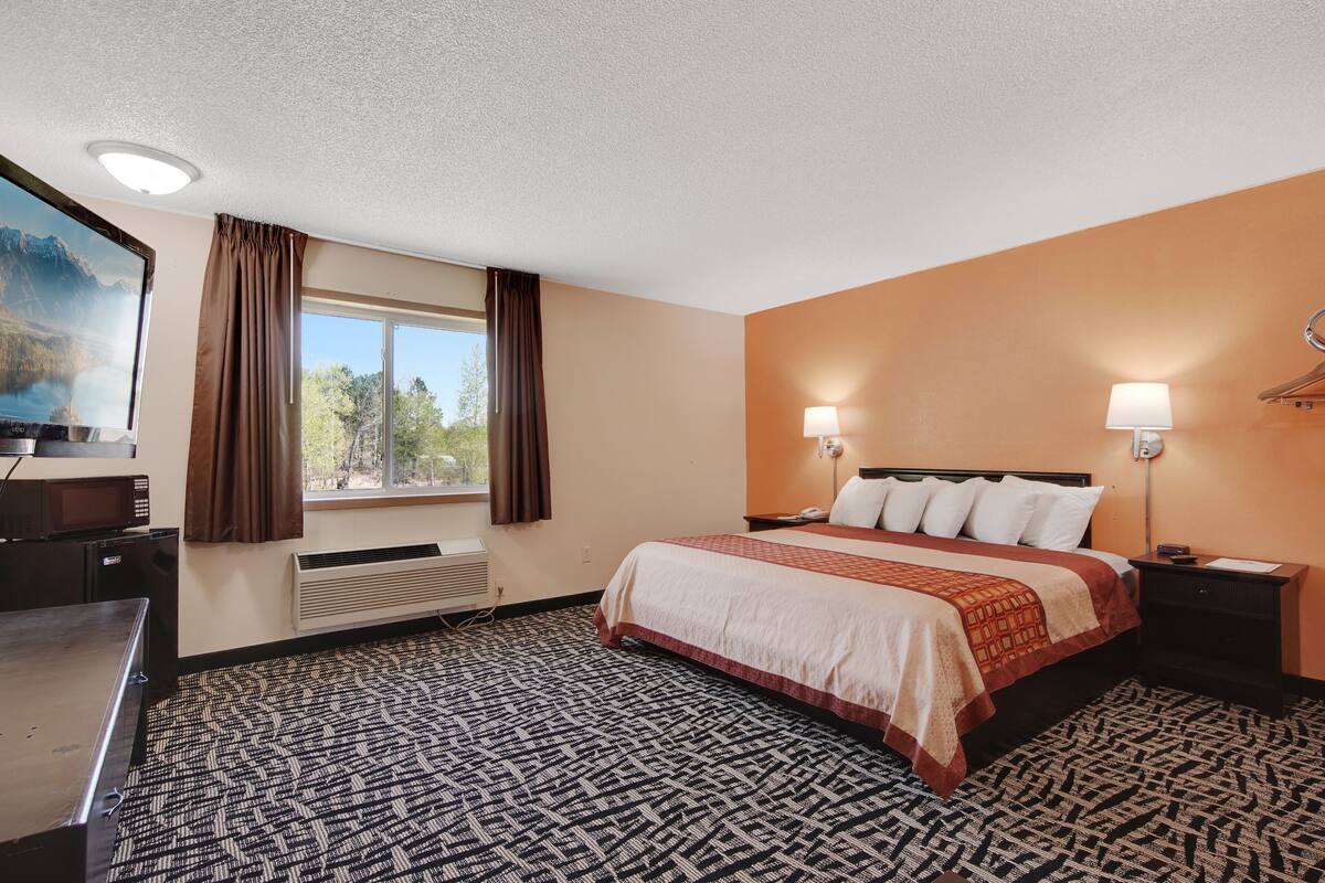 A hotel room with a bed, two bedside lamps, a desk, a television, and a window with curtains.