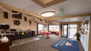 A hotel lobby with a reception desk, a dining area with red chairs, a patterned carpet, and a large blue rug with 'America's Best Hotel' text. - North Town Inn & Suites (Finlayson)