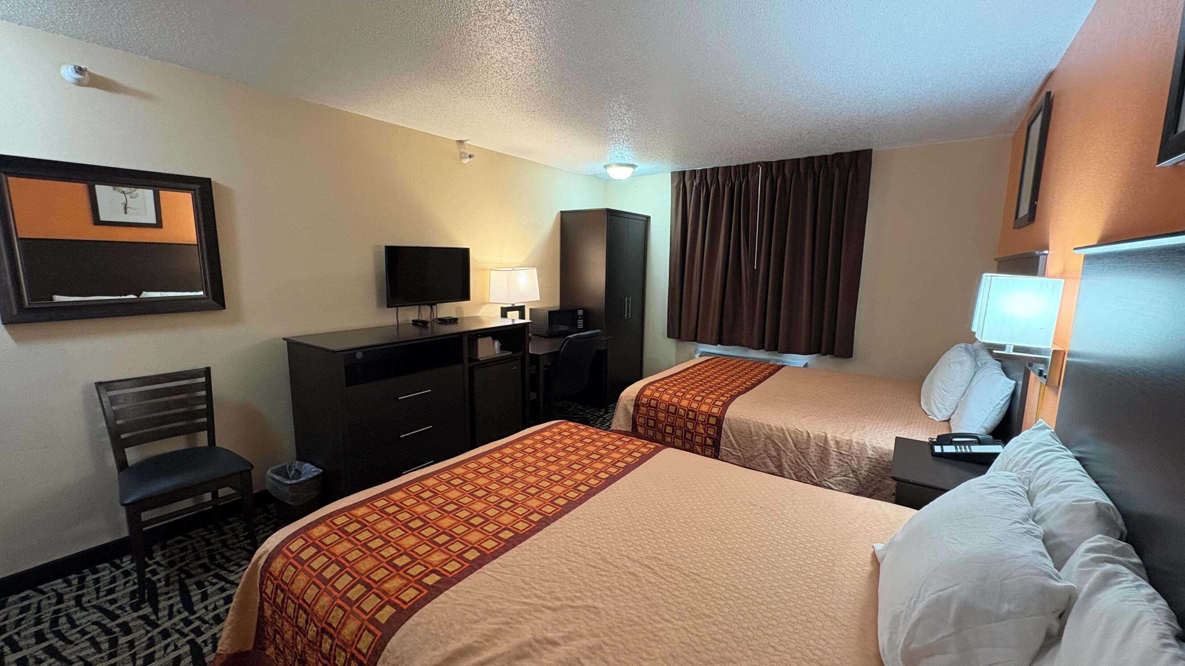A hotel room with two beds, a desk, a television, a mirror, and a window with curtains.
