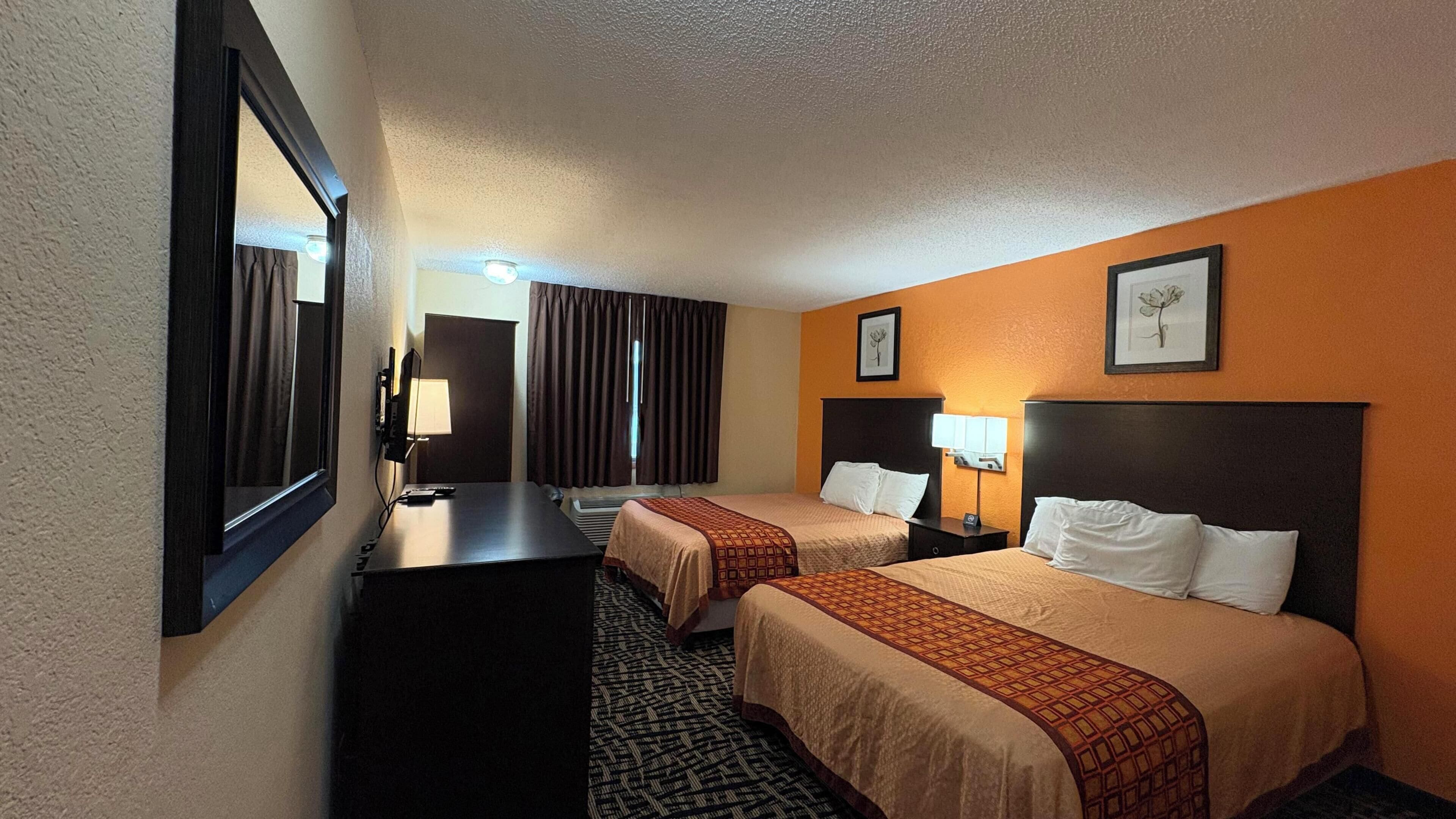 Habitación de hotel con dos camas, un escritorio, un espejo y una ventana con cortinas.