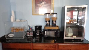 A kitchen counter with a coffee maker, a microwave, a milk dispenser, and a food display. - Welcome Inn (Dallas)