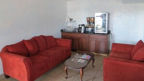 A living room with two red sofas, a coffee table, and a kitchenette with a refrigerator, microwave, and coffee maker. - Welcome Inn (Dallas)
