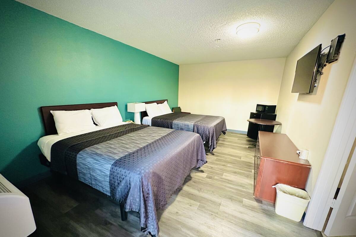 Een hotelkamer met twee bedden, een bureau, een televisie en een prullenbak.