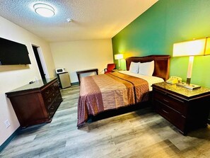 A hotel room with a bed, bedside tables, a desk, a chair, a TV, a microwave, and a green accent wall.