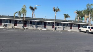 Un motel con una hilera de habitaciones, estacionamiento y palmeras.