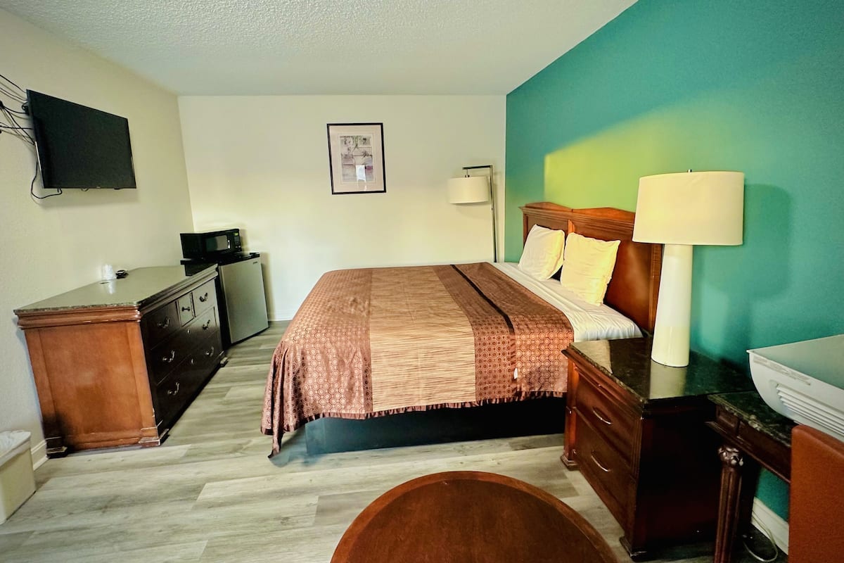 Een hotelkamer met een bed, een bureau, een stoel, een televisie, een foto aan de muur en een lamp.