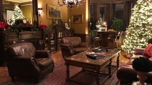 A warmly lit living room with leather armchairs, a coffee table, and a large Christmas tree. - Batcheller Mansion Inn (Saratoga Springs)